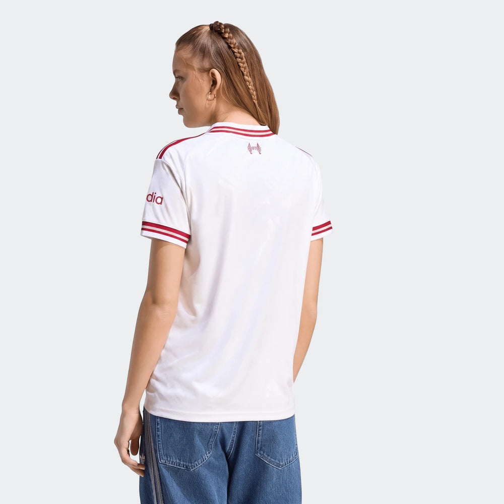 Woman from behind in a white Liverpool FC 26/27 away jersey with red stripes and branding, paired with blue jeans.