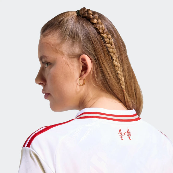 Woman wearing white Liverpool FC 26/27 away jersey with red stripes and '97' flames logo, shown from the back.