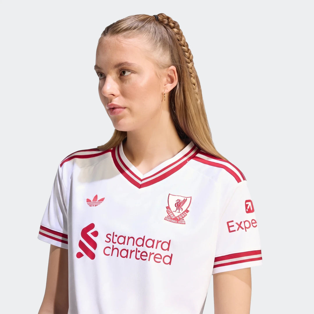 Woman wearing a white Liverpool FC 26/27 away jersey with red sponsor logos and stripes, shown from the waist up.