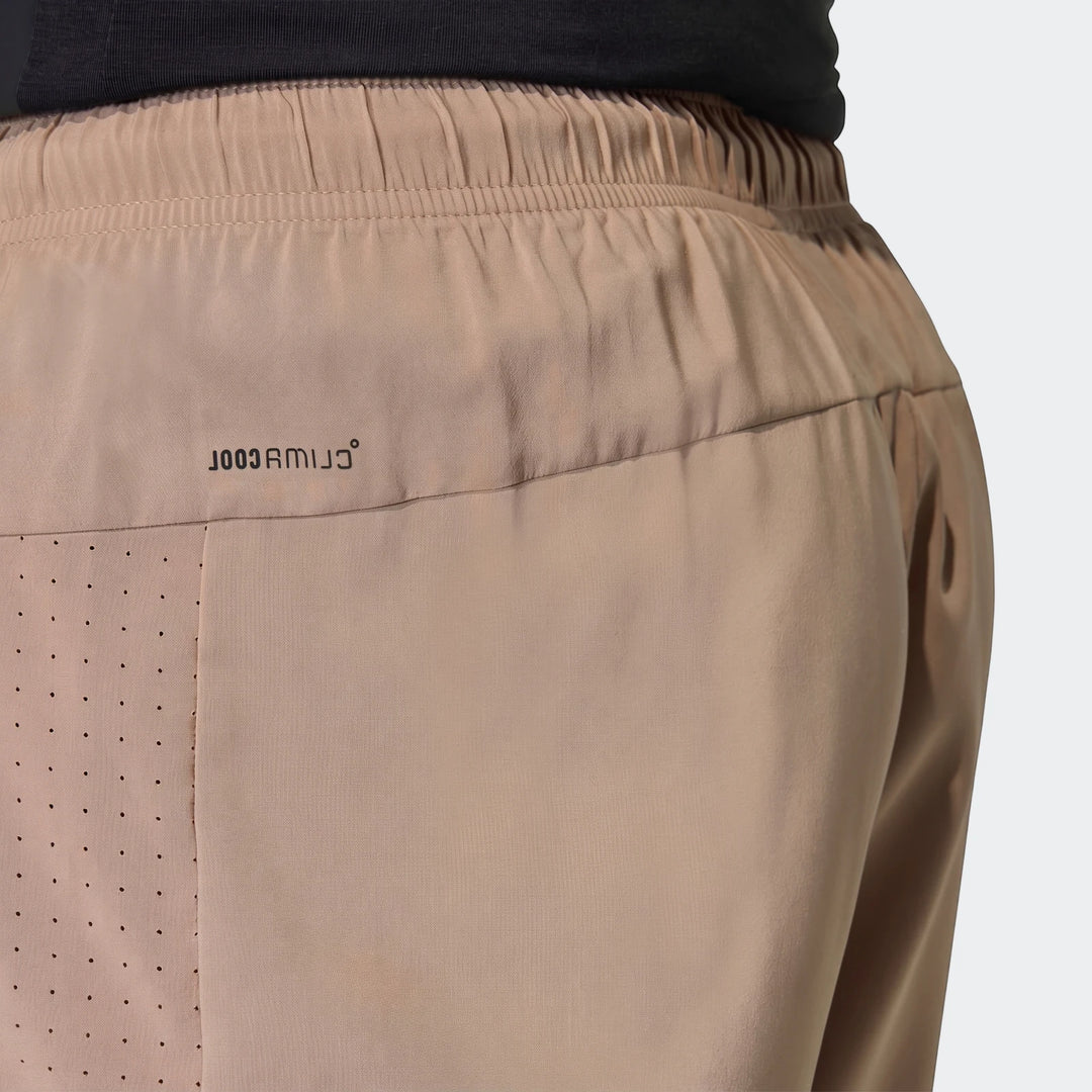 Close-up of beige Workout Essentials Base Woven Shorts featuring an elasticized waistband, perforated panel, and the COOLMAX
