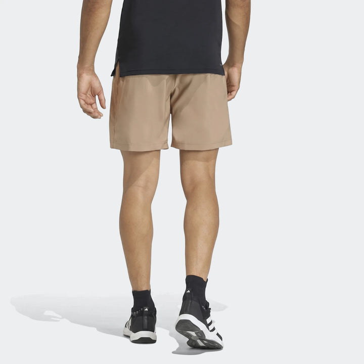 Men's tan Workout Essentials Base Woven Shorts, viewed from the back, worn with black socks and athletic shoes.