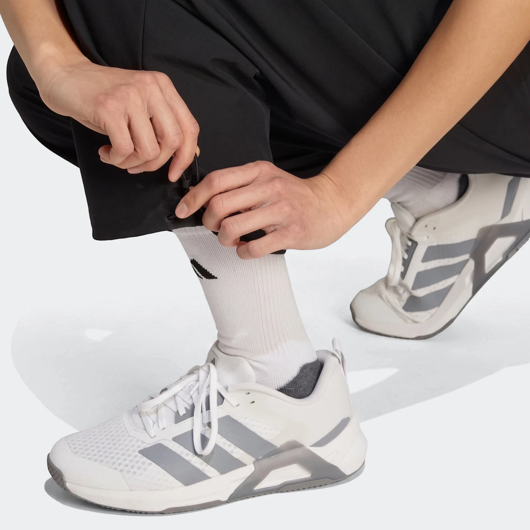 Close-up of a person adjusting the cuff of black Workout Essentials Woven Training Joggers, wearing white socks and white