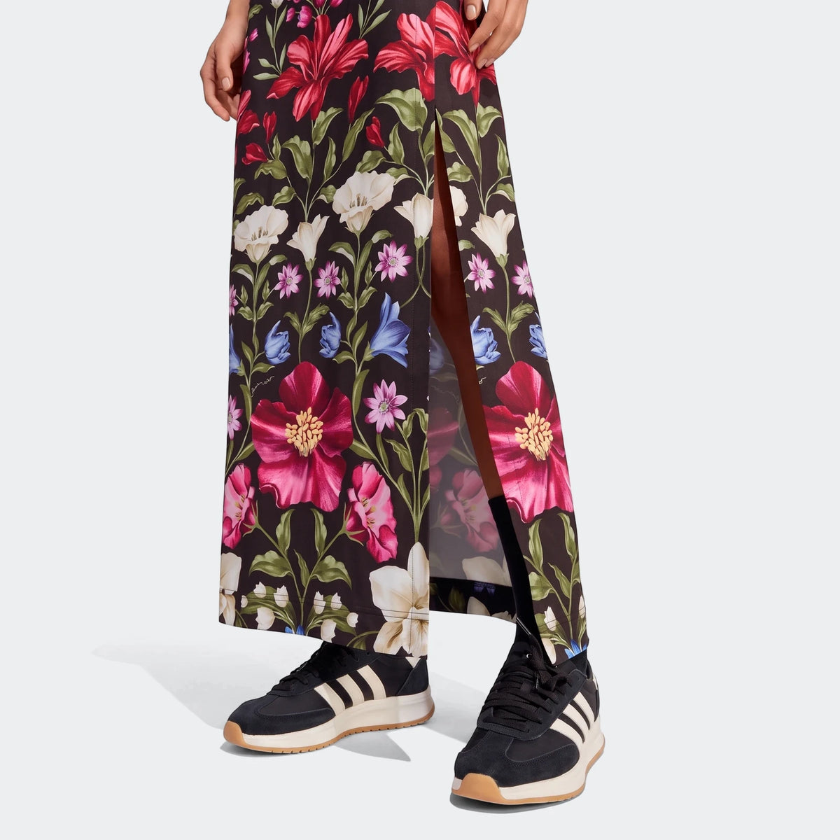 A person wears an X Farm Rio Premium Dress, a long black floral dress with a side slit, paired with black and white sneakers.