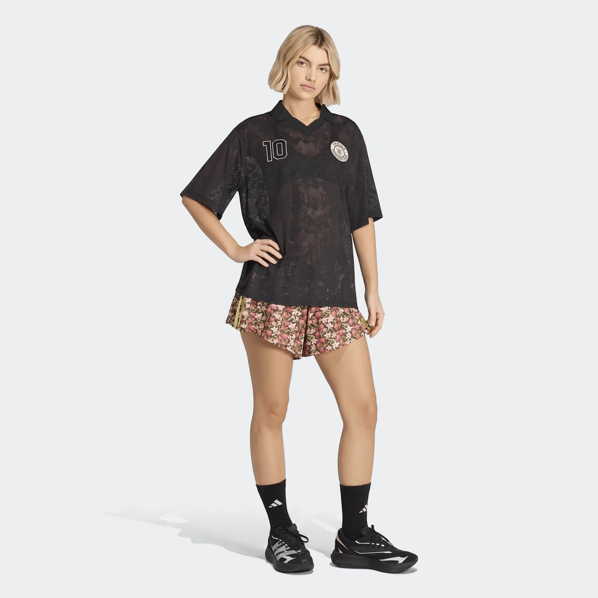 A female model wearing an X Farm Rio Premium Jersey in black with '10' on the front, paired with floral shorts and black