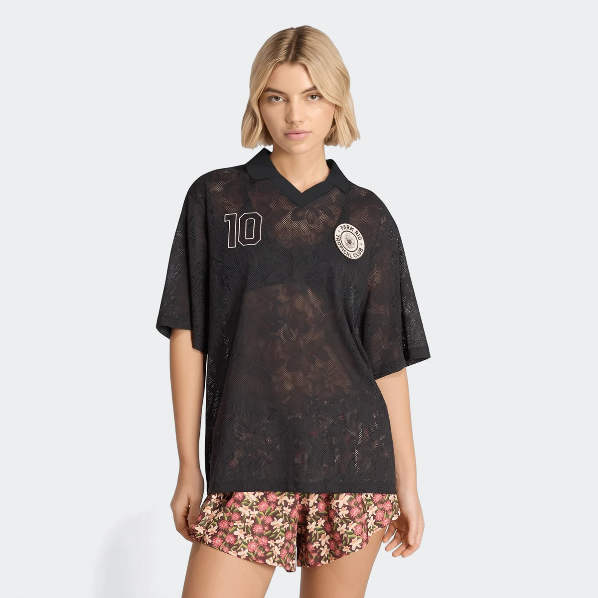A model wears a black X Farm Rio Premium Jersey with a white '10' and a round logo, paired with floral shorts.
