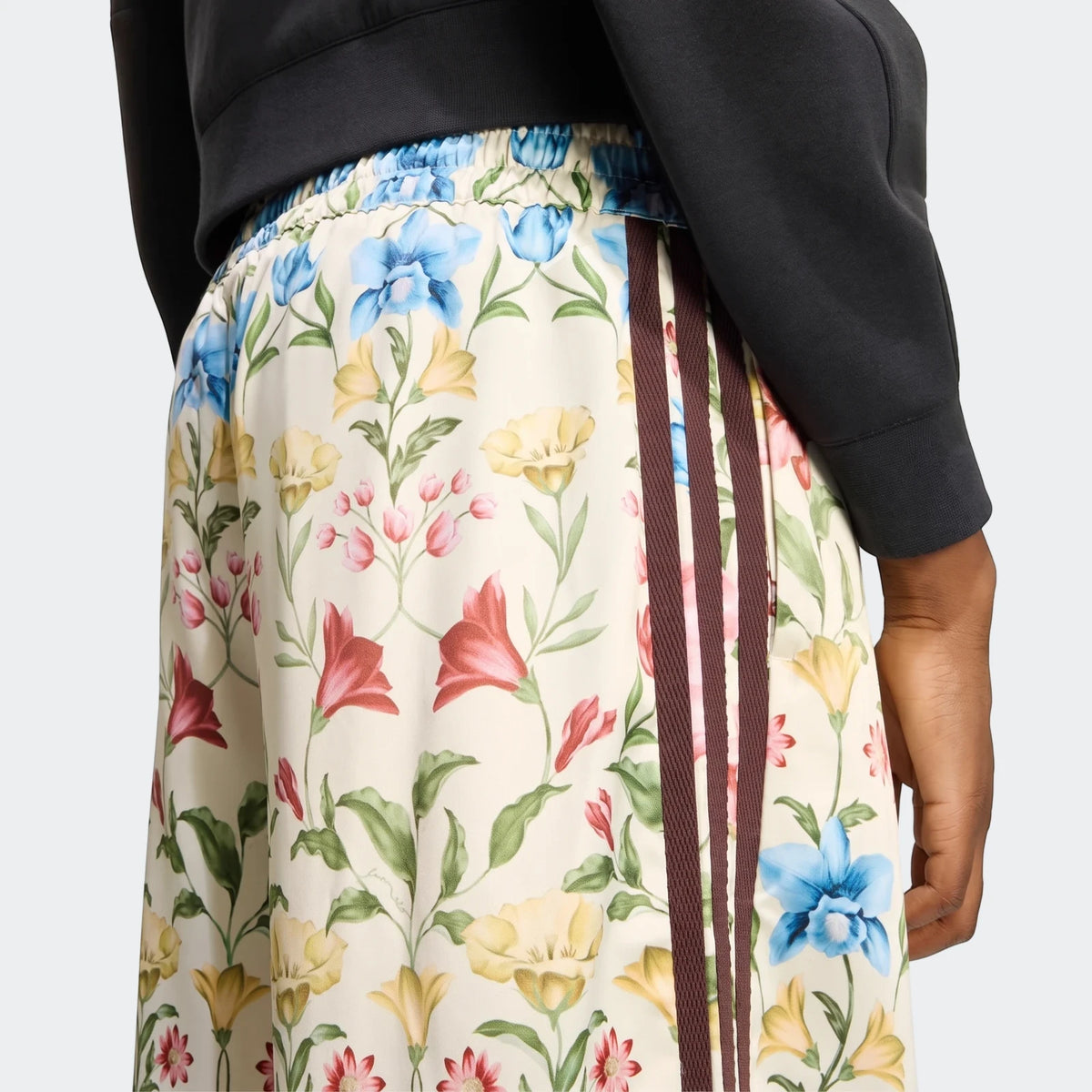 Close-up of X Farm Rio Premium Joggers with a vibrant floral print and brown triple stripes, worn by a person.