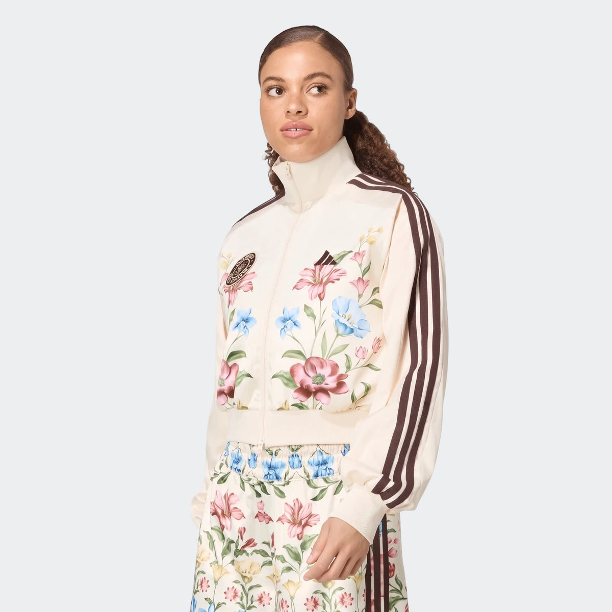 Woman wearing an X Farm Rio Premium Tracktop in cream with a vibrant floral print and dark brown stripes on the sleeves,