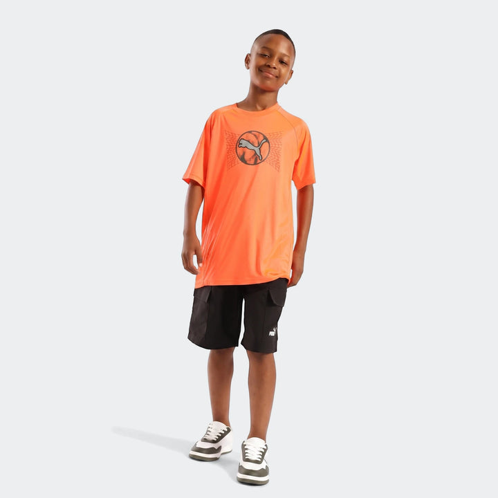 Young boy wearing an orange Puma Active Sports Graphic Tee, black cargo shorts, and two-tone sneakers, full body view.