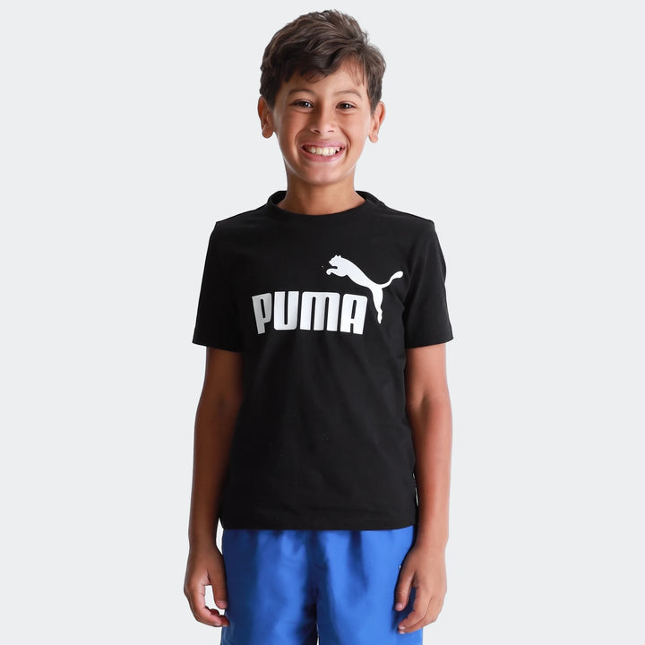 Young boy wearing a black Puma Ess Logo t-shirt and blue shorts, smiling. Front view of a casual outfit.