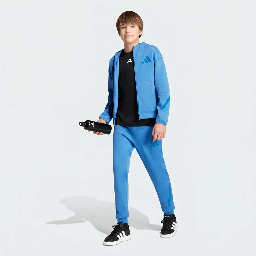 Young boy wearing a blue Adidas Z.N.E. track suit with a black t-shirt and sneakers, holding a water bottle.