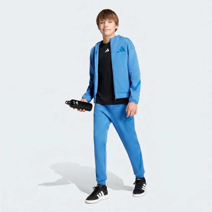 Young boy wearing a blue Adidas Z.N.E. track suit with a black t-shirt and sneakers, holding a water bottle.