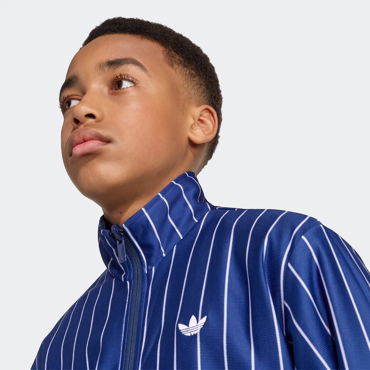 Close-up of a young boy wearing a blue and white striped Adidas Firebird Loose Reversible Tracktop with the Trefoil logo on