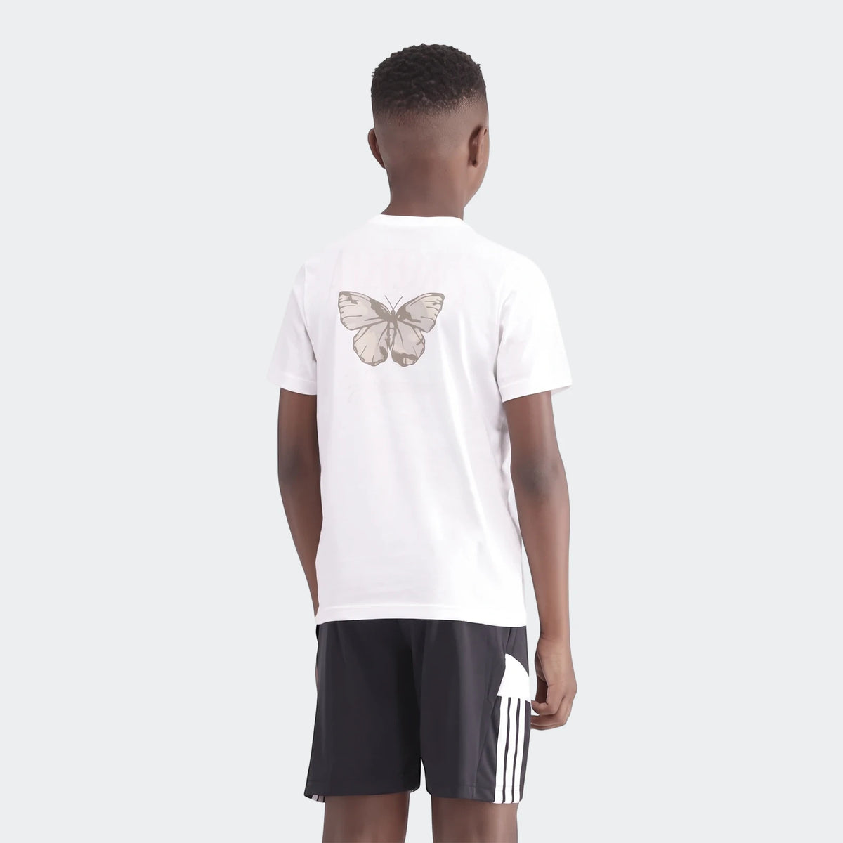 Young boy from behind wearing a white Camo Graphic Tee with a butterfly print and black shorts.