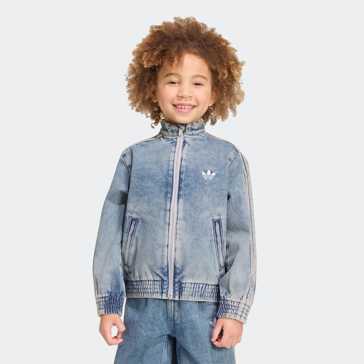 Young child wearing a light wash denim Adidas Firebird Loose Track Top and matching jeans, smiling brightly.