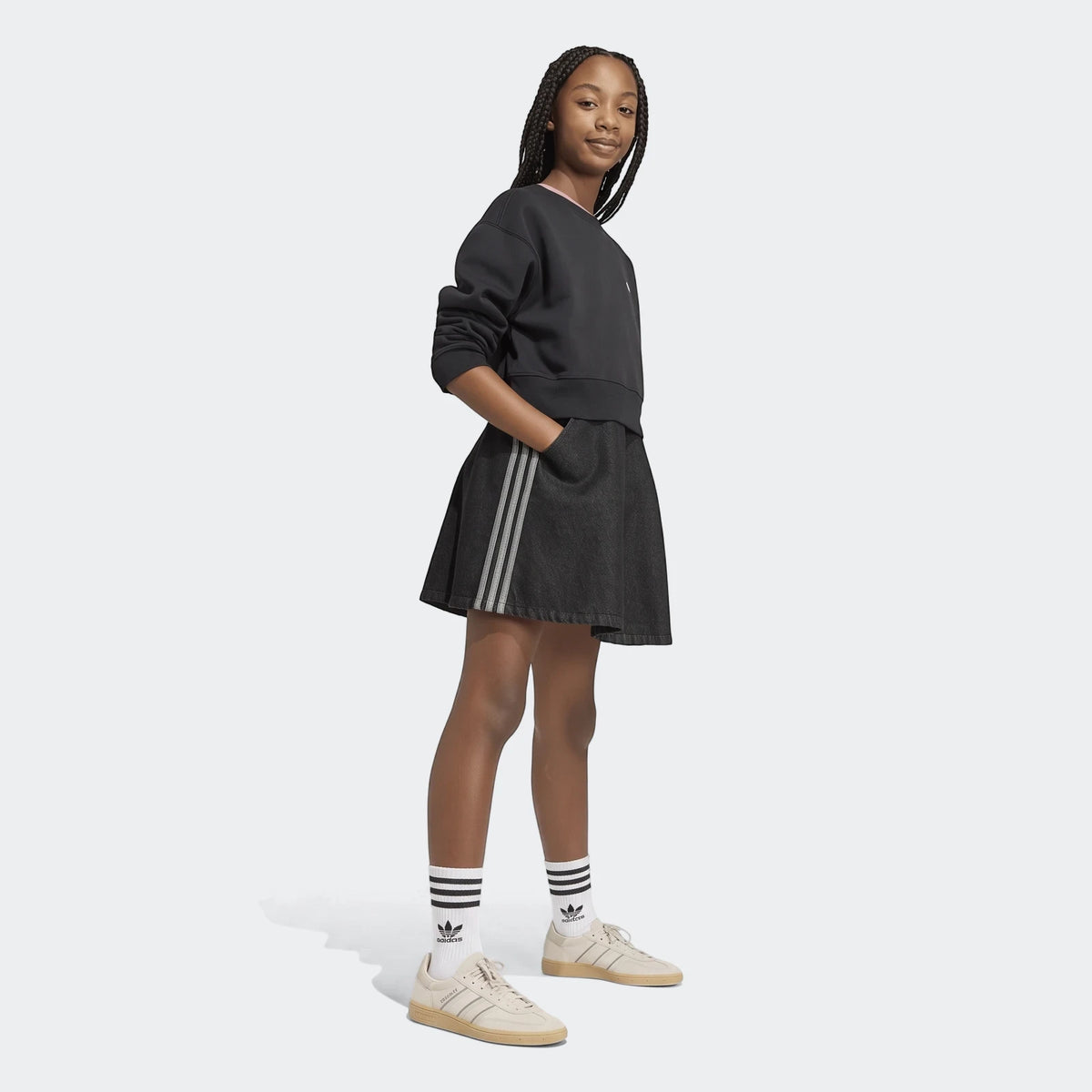 Young girl in black Adidas sweatshirt, dark denim mini skirt with stripes, white socks, and beige sneakers. Full body shot.