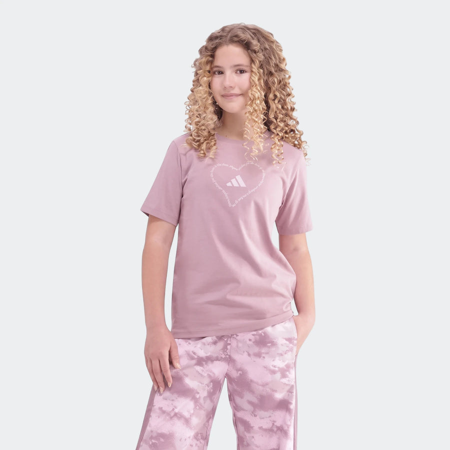 Young girl with curly blonde hair models a purple Adidas Jg Satin T-shirt with a heart logo and purple patterned athletic
