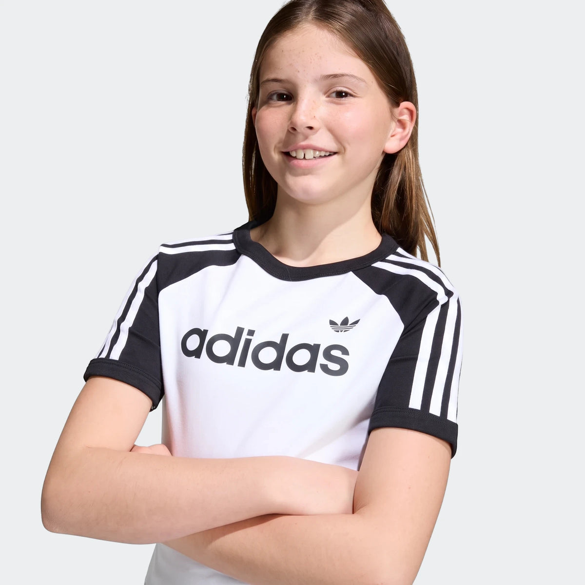 Young girl in a white and black Adidas 3 Stripes Slim T-Shirt with the brand logo and classic sleeve stripes, front view.