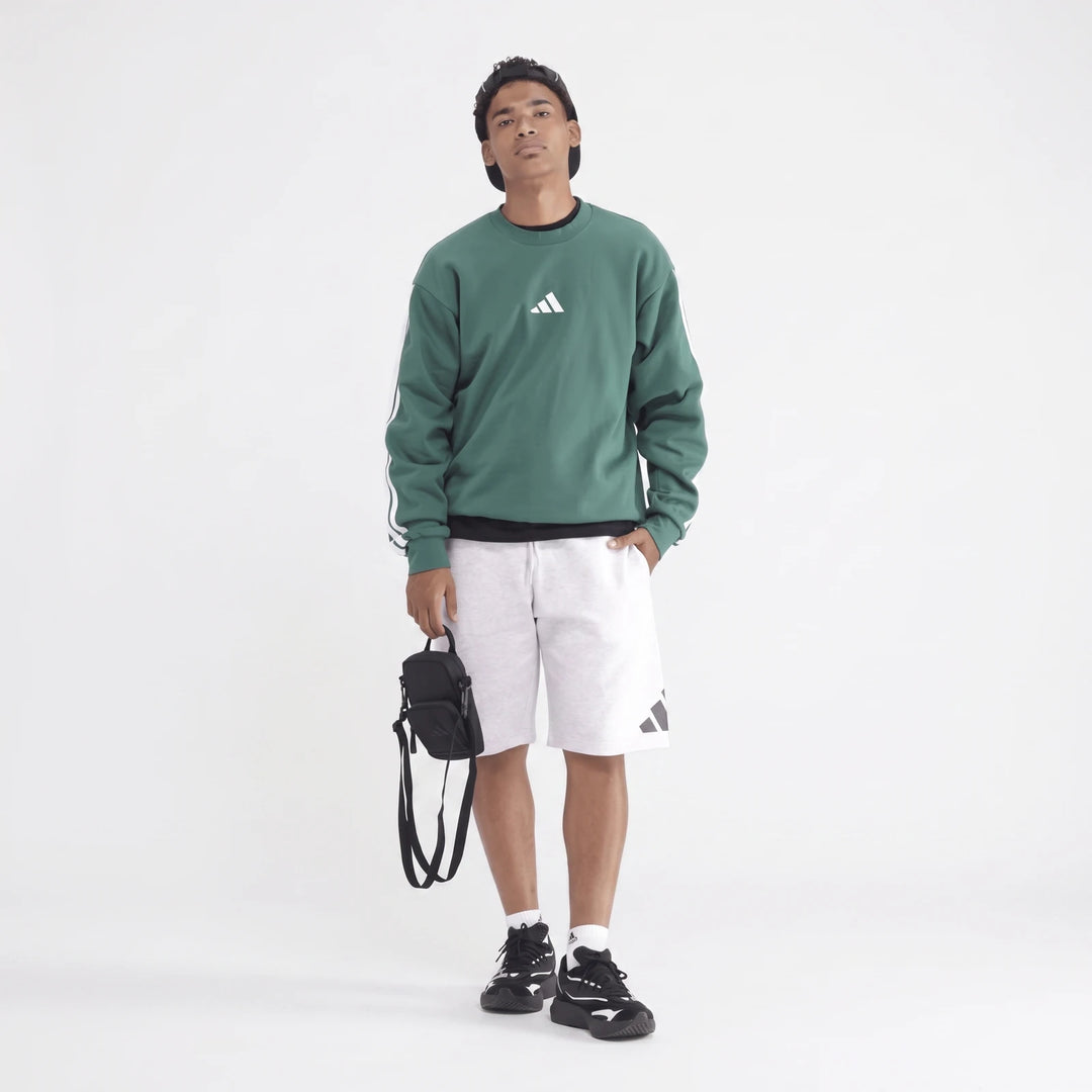 Young man wearing a green long-sleeve sportswear sweatshirt with white stripes, light grey athletic shorts, black and white
