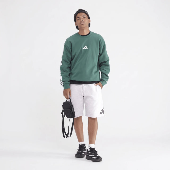 Young man wearing a green long-sleeve sportswear sweatshirt with white stripes, light grey athletic shorts, black and white