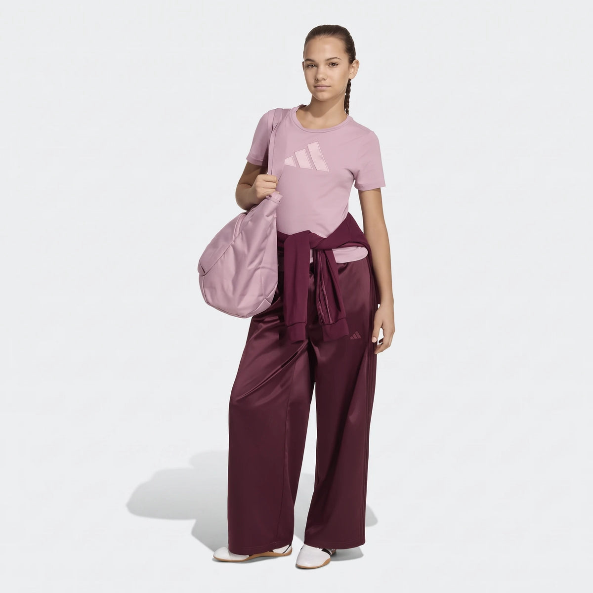 Young woman wearing a pink Adidas Satin T-Shirt, maroon satin wide-leg pants, and a matching sweatshirt, holding a pink