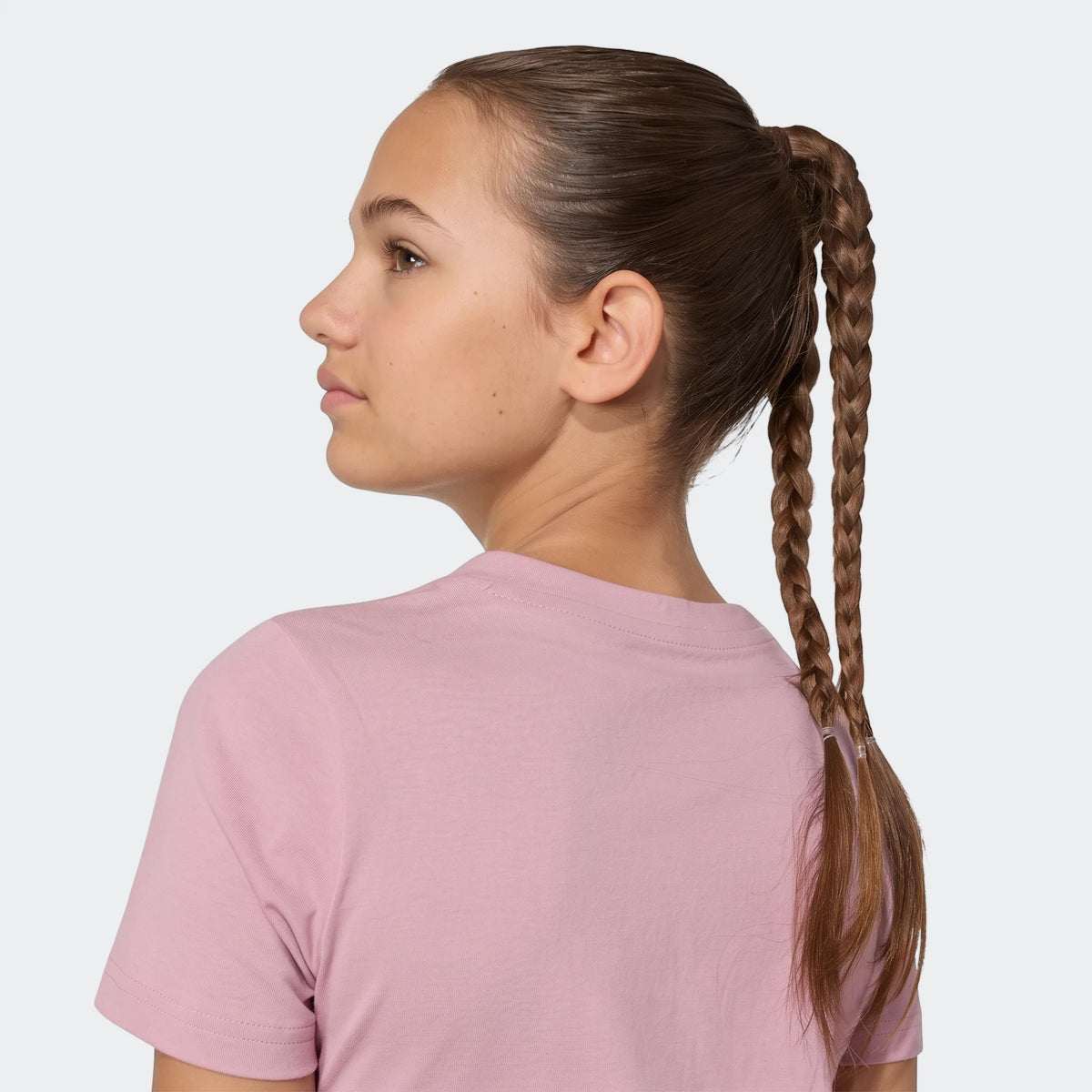 Side view of a young woman wearing a light pink satin t-shirt, her braided hair styled in a high ponytail.