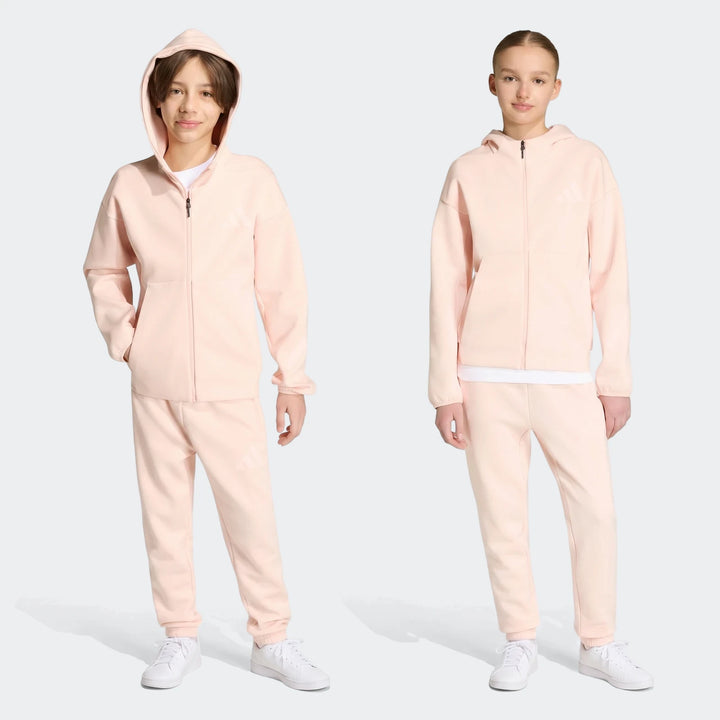 Two youth models wearing light pink Adidas Z.N.E. full-zip hoodies and matching track pants, showcasing a relaxed fit.
