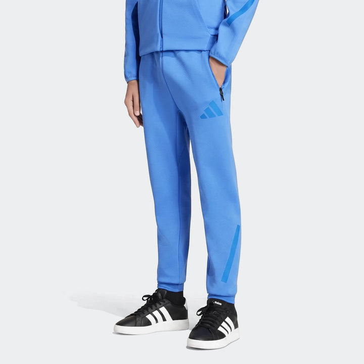 Blue Youth Adidas Z.N.E. Track Pants in a textured knit fabric, shown on a model from the mid-torso down with black and