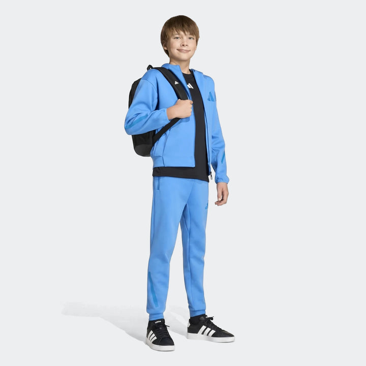 Full body image of a young boy wearing a blue Youth Z.N.E. full-zip hoodie and matching blue joggers, paired with a black