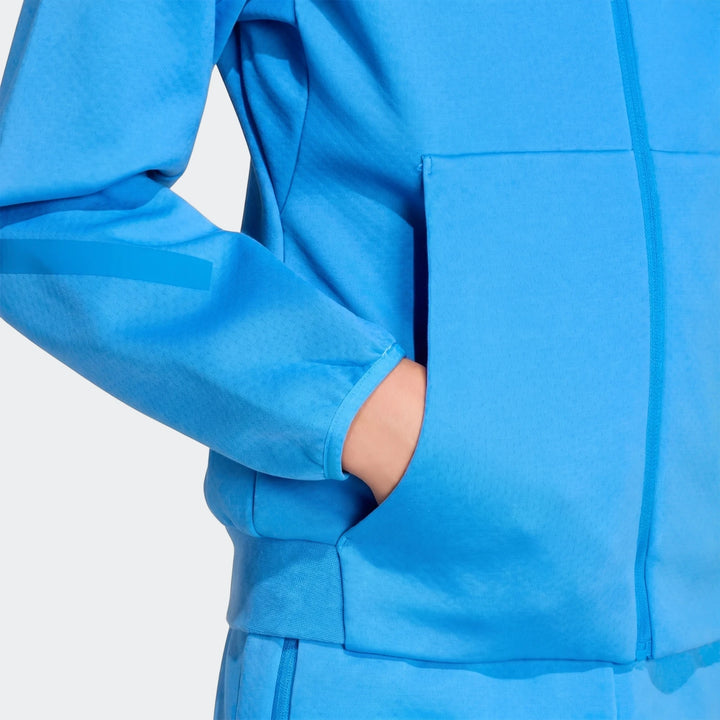 Close-up of a youth wearing a bright blue Adidas Z.N.E. Full-Zip Hoodie, with their hand comfortably placed in the front
