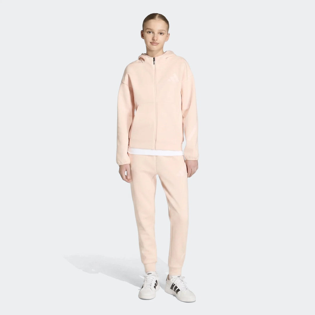 Young female model wearing a light pink Youth Z.N.E. Full-Zip Hoodie and matching joggers with white sneakers, full body