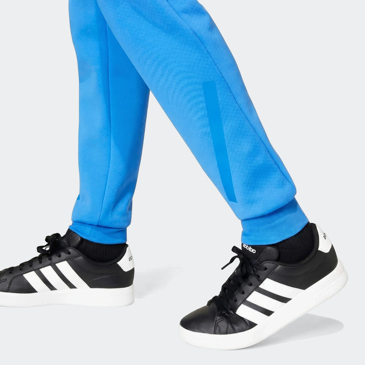 Close-up of a person wearing blue Adidas Youth Z.N.E. Track Pants with black and white Adidas sneakers.