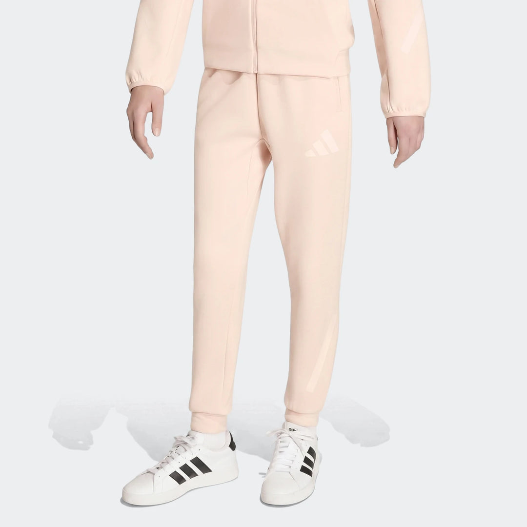 Youth Z.N.E. Track Pants in light pink with white Adidas logo, paired with white sneakers and black stripes on a model.