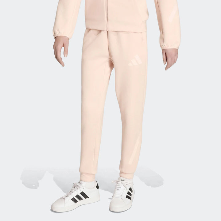 Youth Z.N.E. Track Pants in light pink with white Adidas logo, paired with white sneakers and black stripes on a model.