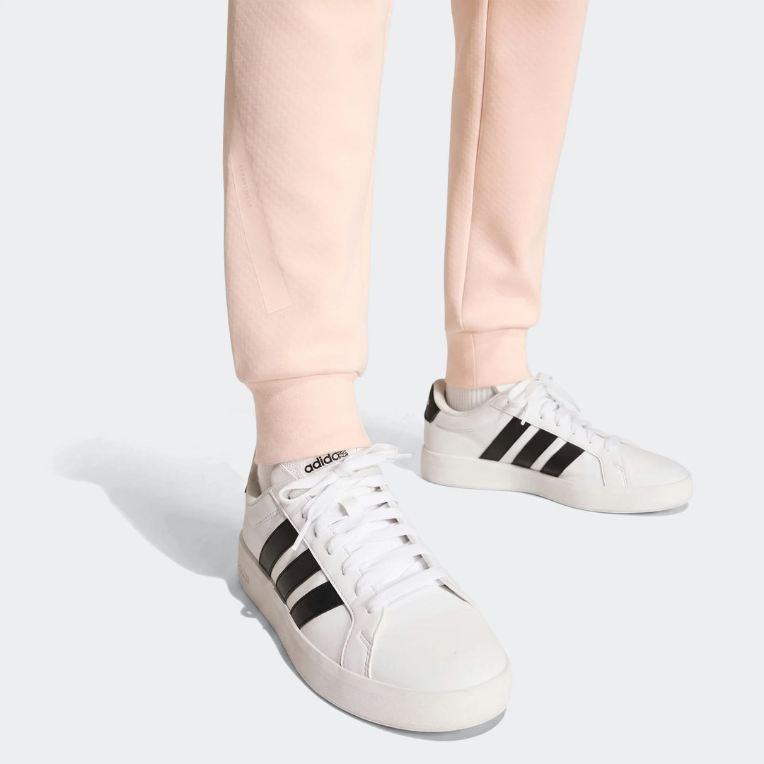 Close-up of light pink Youth Z.N.E. track pants with ribbed cuffs, worn with white Adidas sneakers featuring black stripes