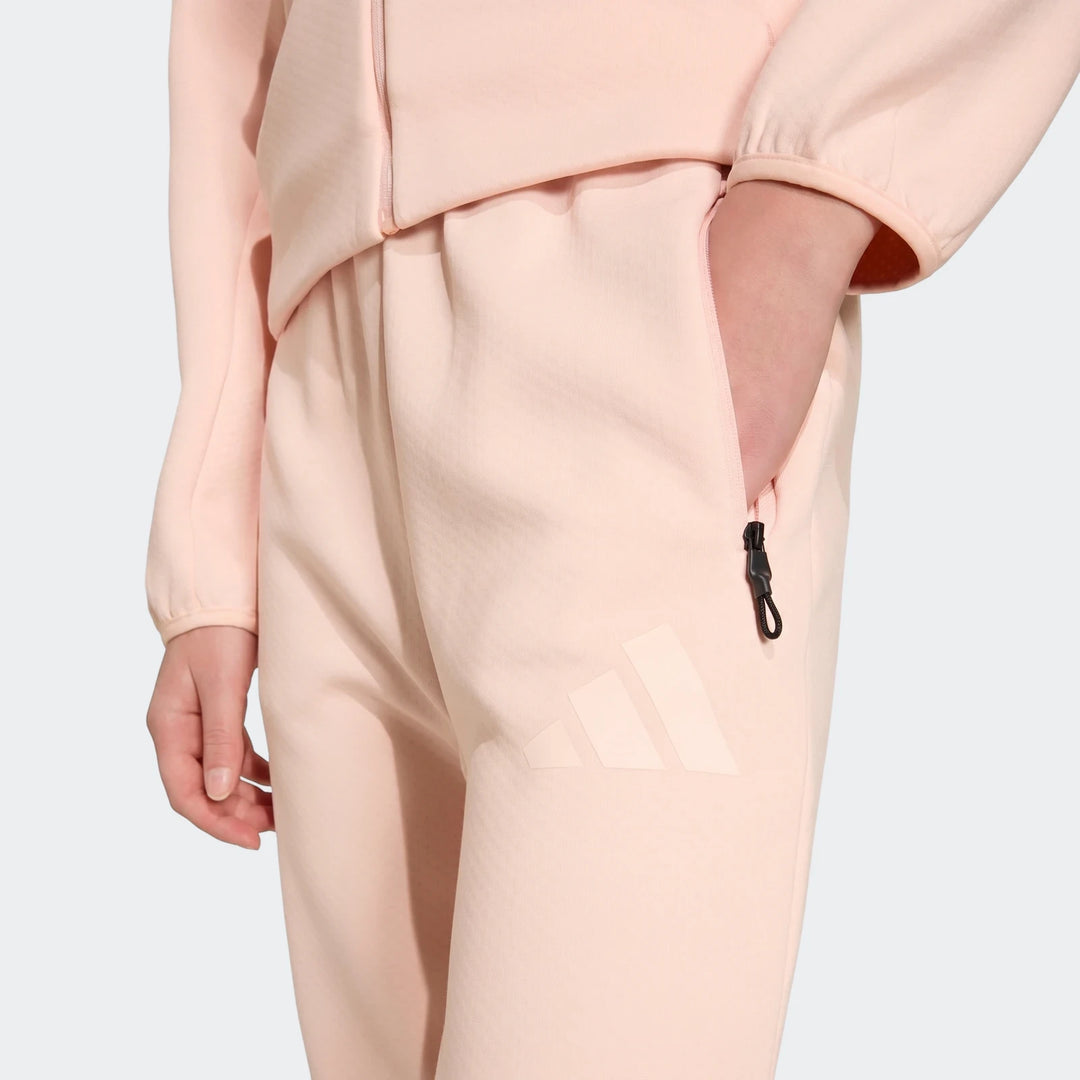 Close-up of a person wearing pink Adidas Youth Z.N.E. track pants, with a hand in the pocket and visible logo.