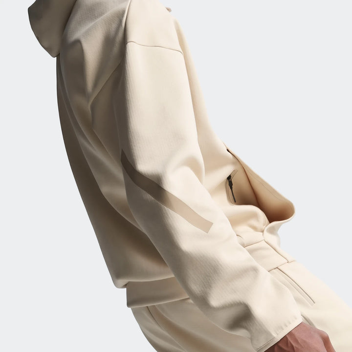 Close-up of a person wearing a light beige Z.N.E. Full-Zip Hoodie and matching pants, showcasing the zippered pocket and