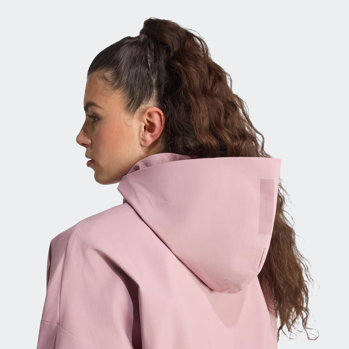Woman wearing a pink Z.N.E. Woven Track Top with a hood, viewed from the back and side in profile.