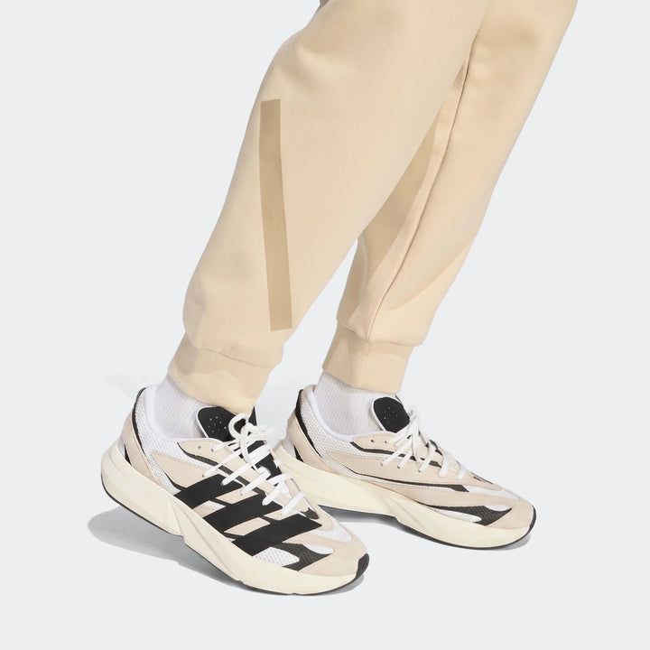Beige Z.N.E. Track Pants with a relaxed fit, worn by a person standing in black and white athletic sneakers.
