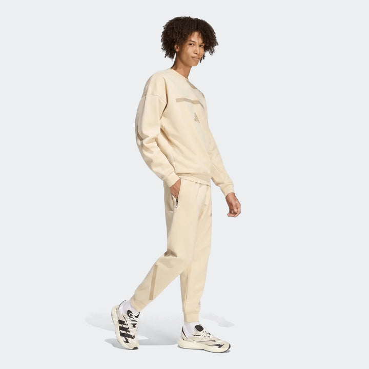 Z.N.E. Track Pants in light beige with tapered legs and zip side pocket, shown from a side view on model.