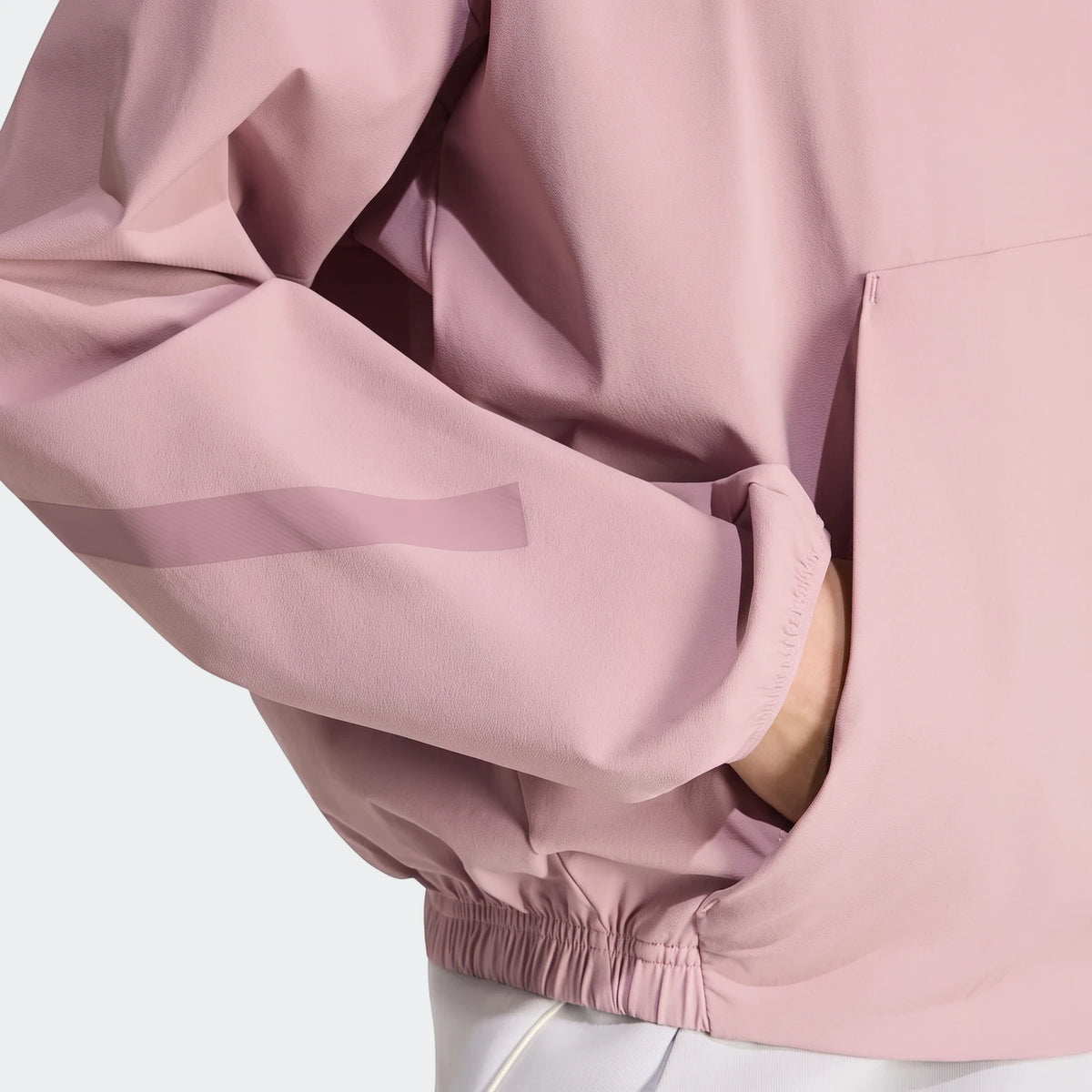 Close-up of a pink mauve Z.N.E. Woven Track Top, highlighting the woven fabric, side pocket, and a translucent sleeve detail.